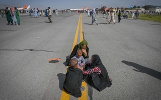 Naisia ja lapsia istumassa maassa lentokentän kiitoradalla.
