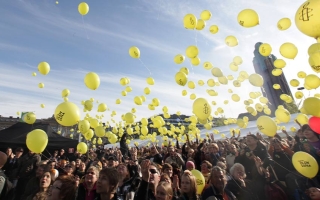 Joukko ihmisiä päästää keltaisia ilmapalloja käsistään kohti taivasta.