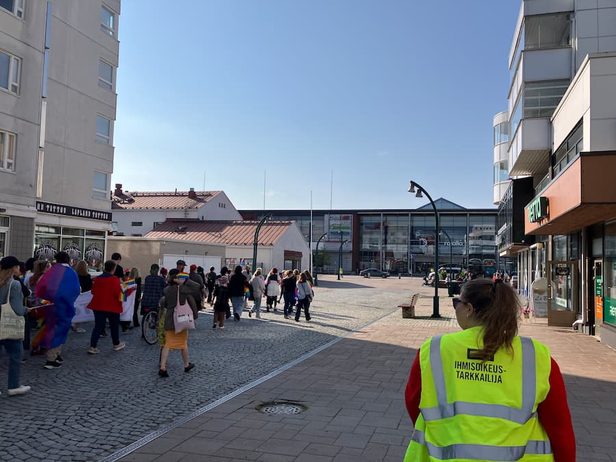 Mielenosoituskulkue. Etualalla mielenosoitustarkkailijana toimiva ihminen, jolla päällä keltainen ihmisoikeustarkkailija-liivi.