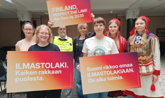 Valokuva järjestöjen edustajista pitelemässä ilmasto-oikeudenkäyntiin liittyviä kylttejä.